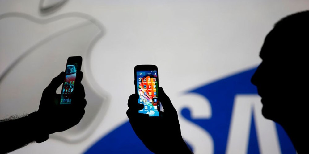 Men are silhouetted against a video screen with Apple and Samsung logos as he poses with Samsung S3 and Samsung S4 smartphones in this photo illustration taken in the central Bosnian town of Zenica